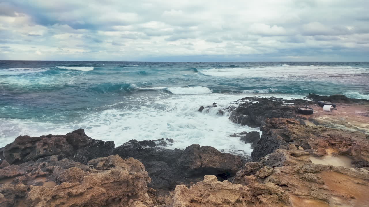 Le onde si infrangono con forza sulle rocce costiere, spruzzando acqua in aria, sotto un cielo nuvoloso