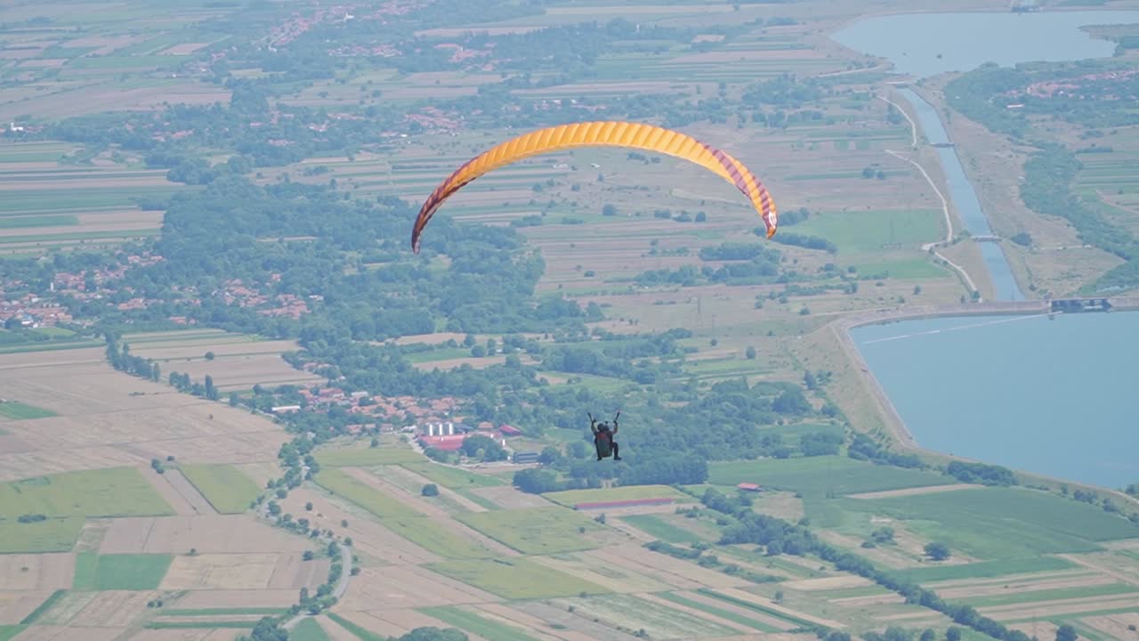 Paragliders float gracefully in the wind, surrounded by a bright, clear sky and a stunning landscape below.