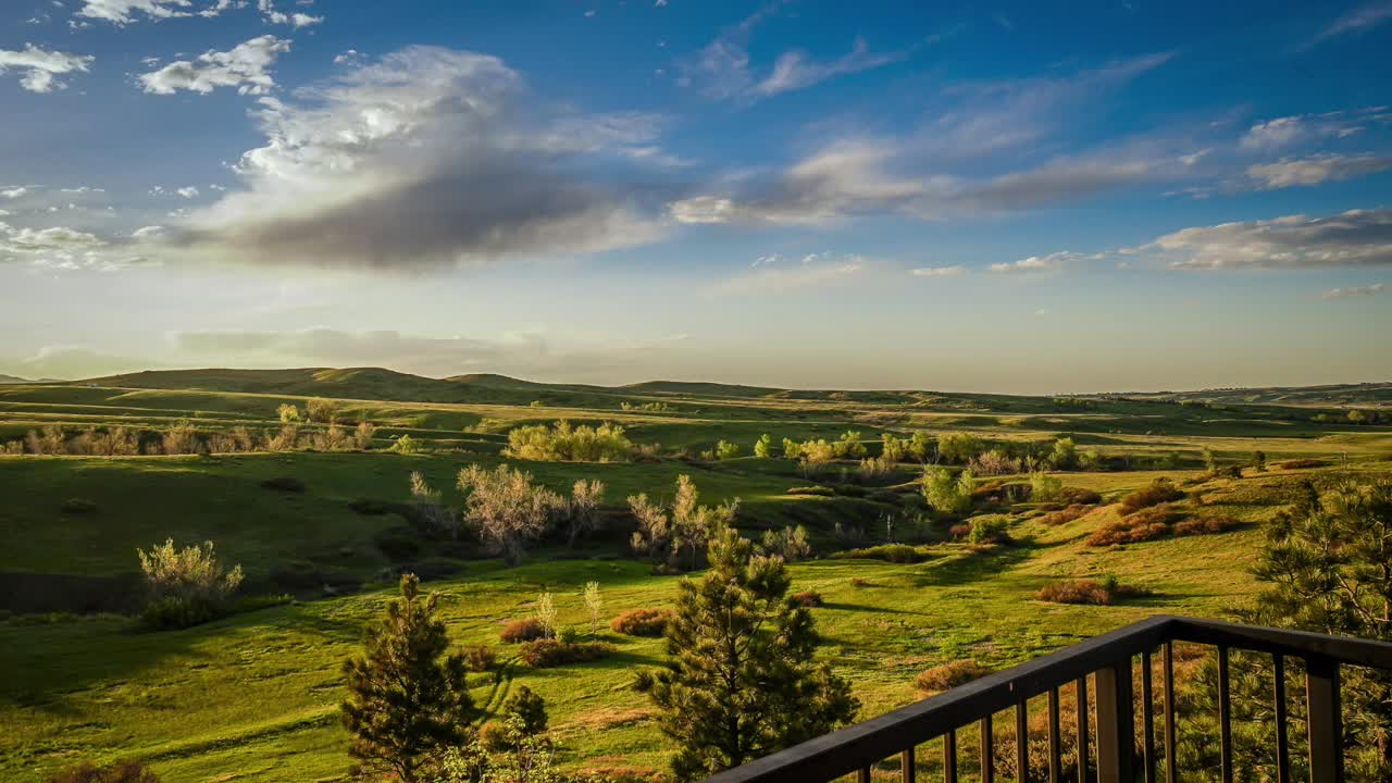 Time lapse of afternoon clouds and shadows moving across rolling green hills in Colorado Springs, Colorado. Porch railing in frame.
