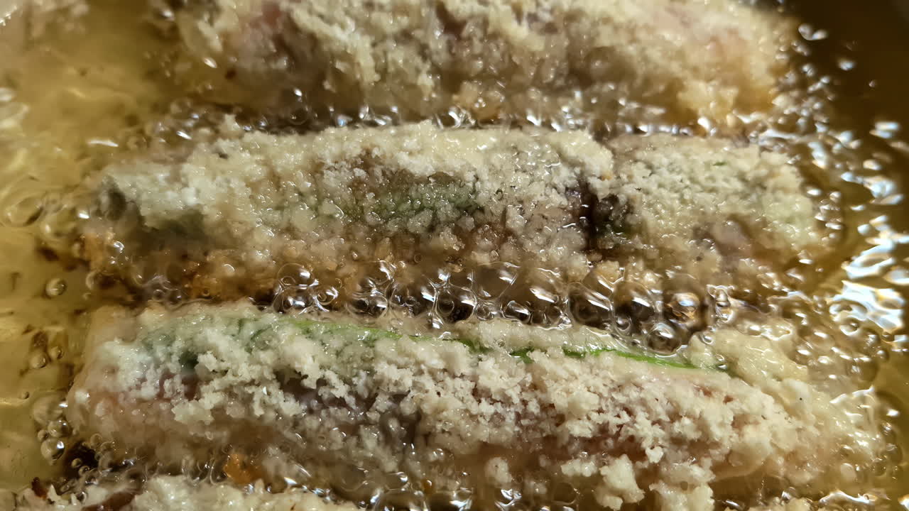 Slow zoom-out reveals golden-battered homemade sushi rolls sizzling and bubbling in hot oil on a stovetop