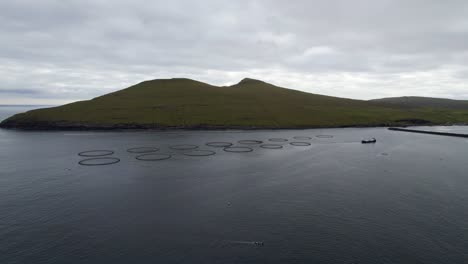 Aerial-panorama-view-of-salmon-farm-and-fishing-boats-on-coastline-of-Sandavagur,-Faroe-Islands