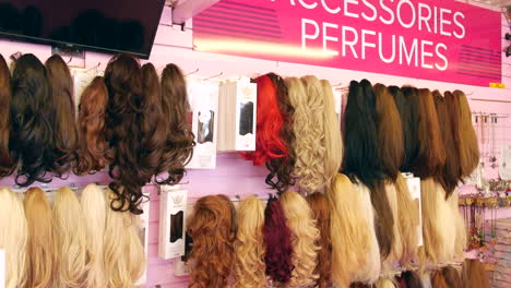 wigs and hair extensions in various shades, from blonde to brunette, is displayed in a shop. the synthetic hairpieces range from straight to curly, offering a wide selection of styles and colors