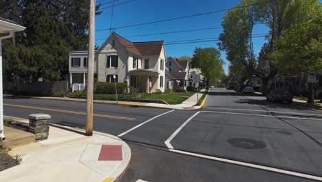 drone flight on street in american housing area during sunny day with blue sky. parking cars and blooming trees.