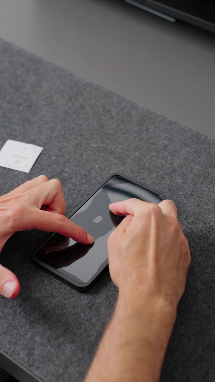 Persona che applica una pellicola protettiva in vetro temperato trasparente sullo schermo di uno smartphone, garantendo protezione e manutenzione del dispositivo