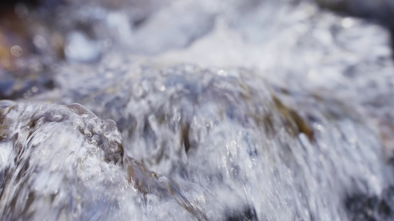 Close-up of clear, rushing water over rocks. Water splashes and bubbles in natural light. Perfect for nature, travel, or wellness content. High detail, dynamic motion, fresh and pure feel