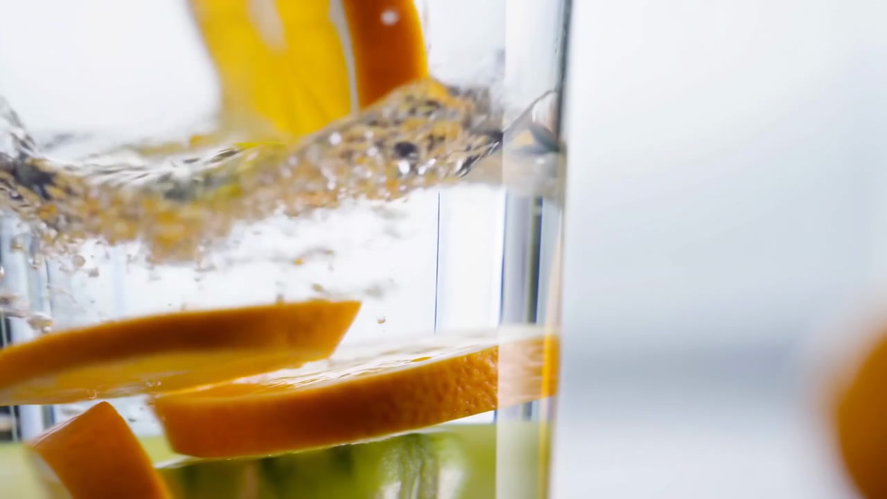 Fette di agrumi che si tuffano nell'acqua, primo piano luminoso in studio che mostra fette di arancia e lime che creano un effetto energico