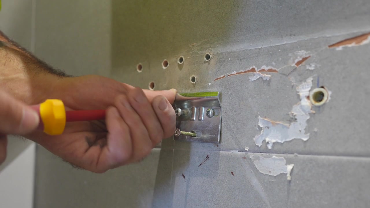 Male hands of a craftsman using a screwdriver to fix a metal plate on a tiled wall