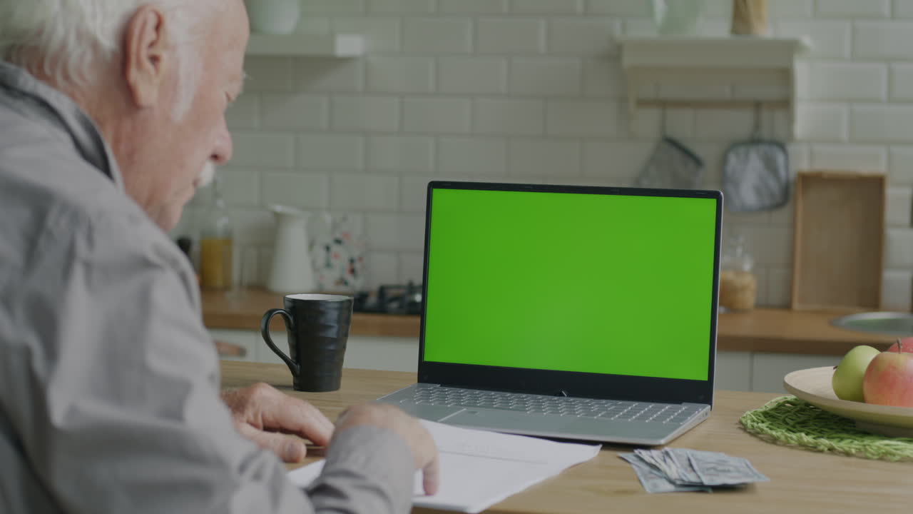 Elderly Man Working on Laptop in Kitchen