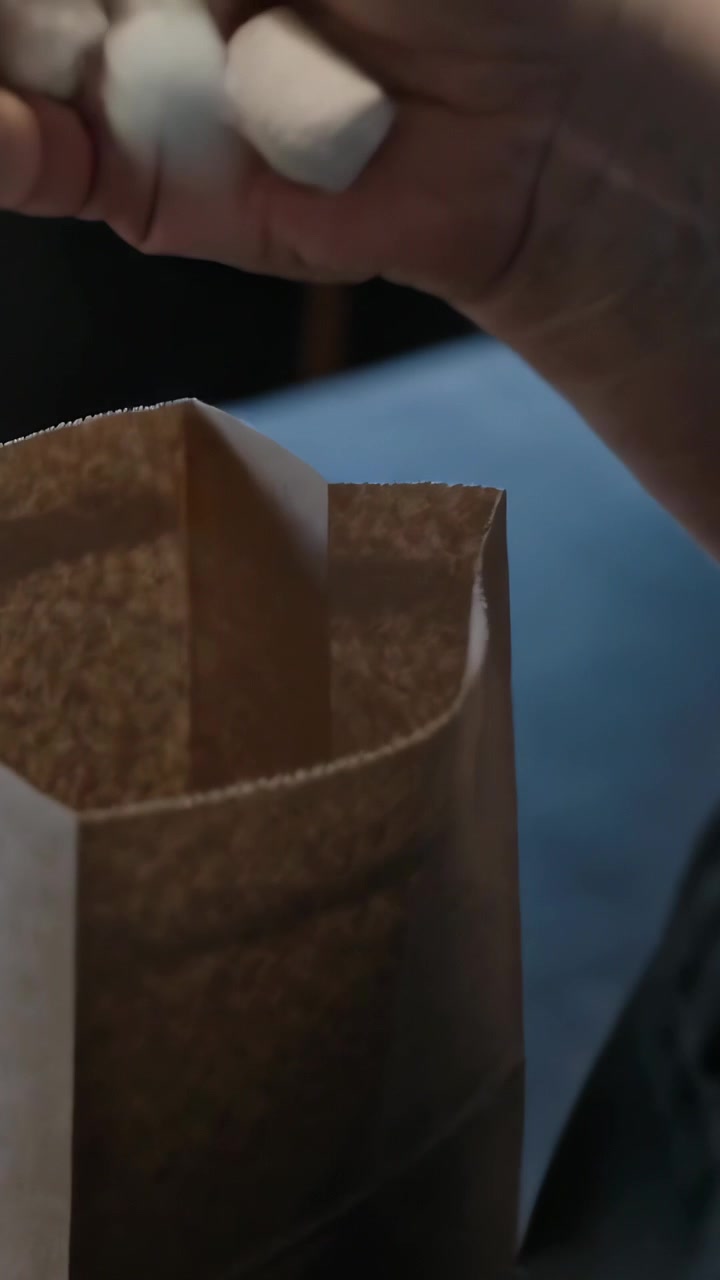 Vertical video: Using hands, surgical mask adult collecting white cylinders into brown bag at seat