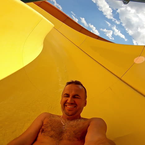 joyful male going down from yellow pipe outdoors. man having fun and sliding down in a water slide in summer at a sunny day.