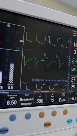 the screen of artificial lung ventilation apparatus working during surgery. black monitor demonstration life signs of a patient under procedure. doctors operating at backdrop. vertical video