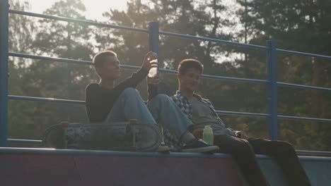 two friends sitting in skate park talking while drinking water