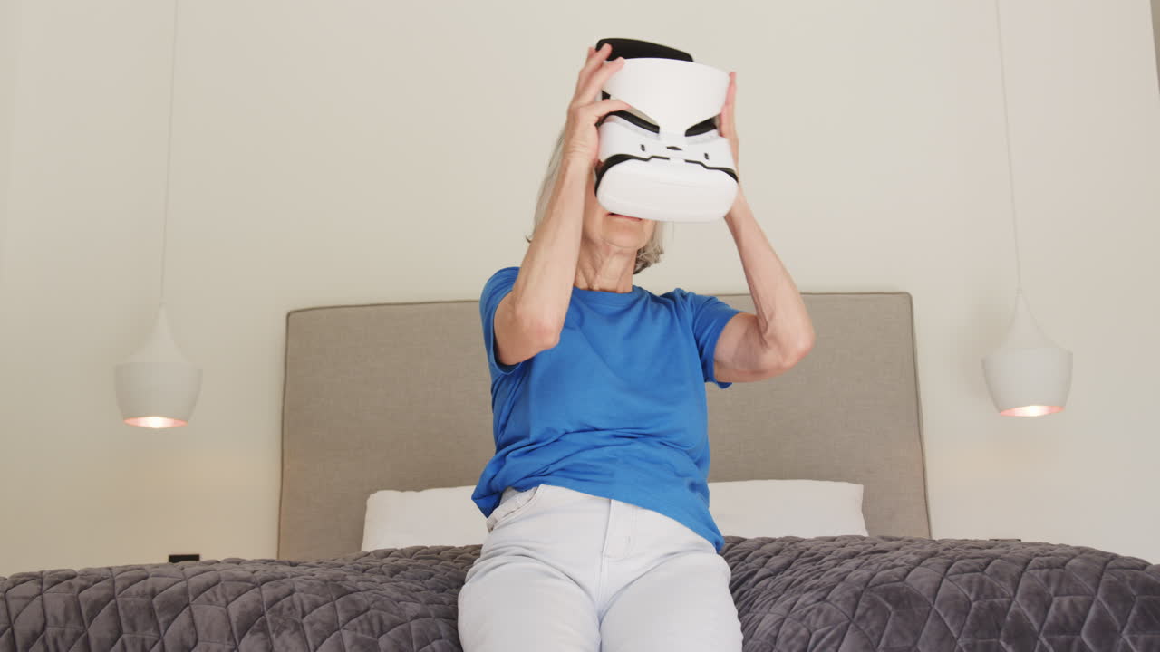 Senior woman exploring virtual reality headset while sitting on bed at home