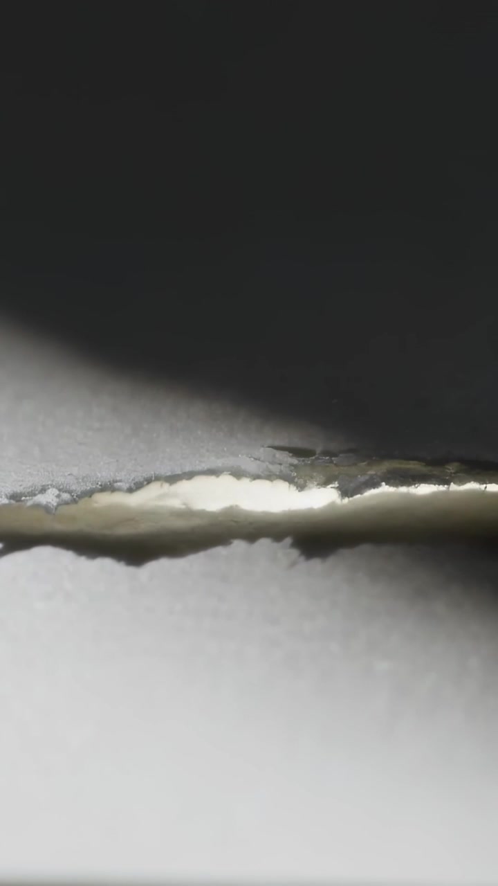 Vertical video: Moving shadow revealing tear in white paper in studio, showing light, fibrous edges