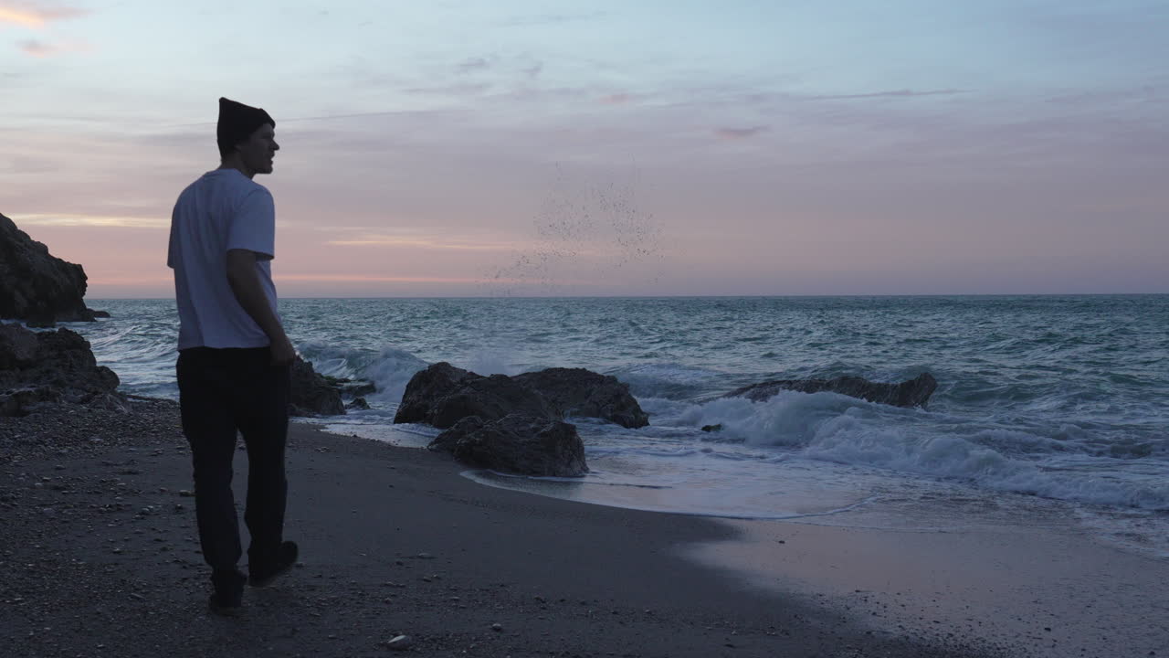 Uomo in camicia bianca passeggia lungo la costa dell'oceano al tramonto, scatta una foto del mare