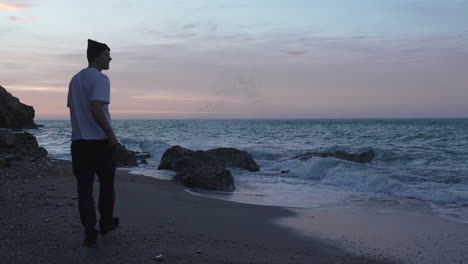 man in white shirt walks along the ocean coast during nightfall, takes photo of sea