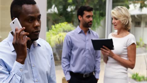 Executive-talking-on-mobile-phone-while-colleagues-using-digital-tablet