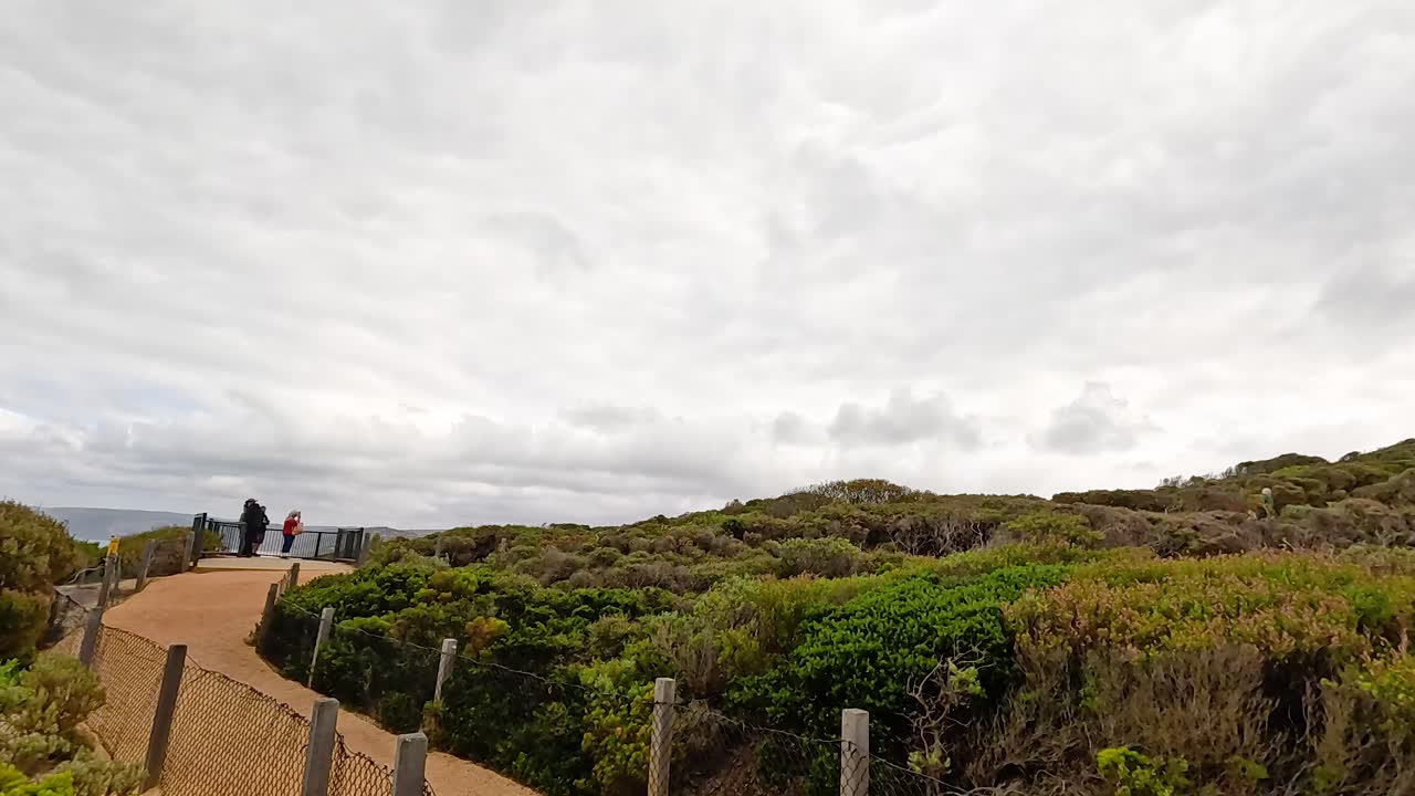 A serene walk along a coastal path leading to a lighthouse under overcast skies at Aireys Inlet, Victoria