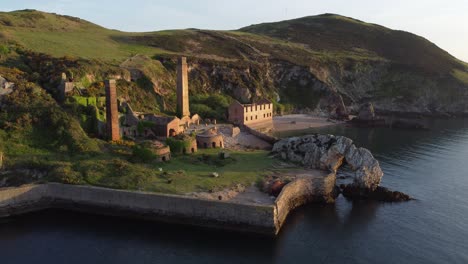 Porth-Wen-abandoned-coastal-derelict-brickworks-remains-golden-sunrise-countryside-bay-aerial-view-fast-left-orbit