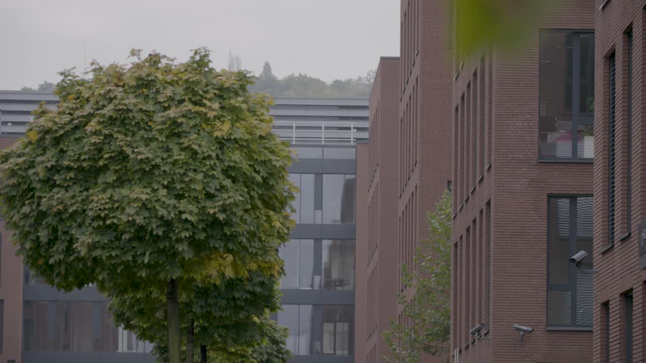 Modern office buildings with brick facades and lush green trees on an overcast day