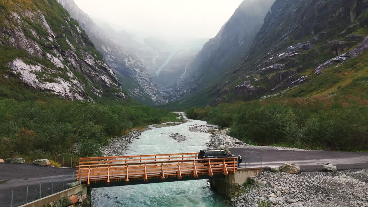 Car crossing a bridge with the Kjendalsbreen glacier in the background (drone footage)