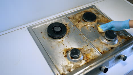 cleaning a dirty stove. a person wearing a blue glove cleans a grimy stove top in a well-lit kitchen during the day