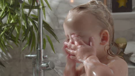 baby girl washing face from bath foam