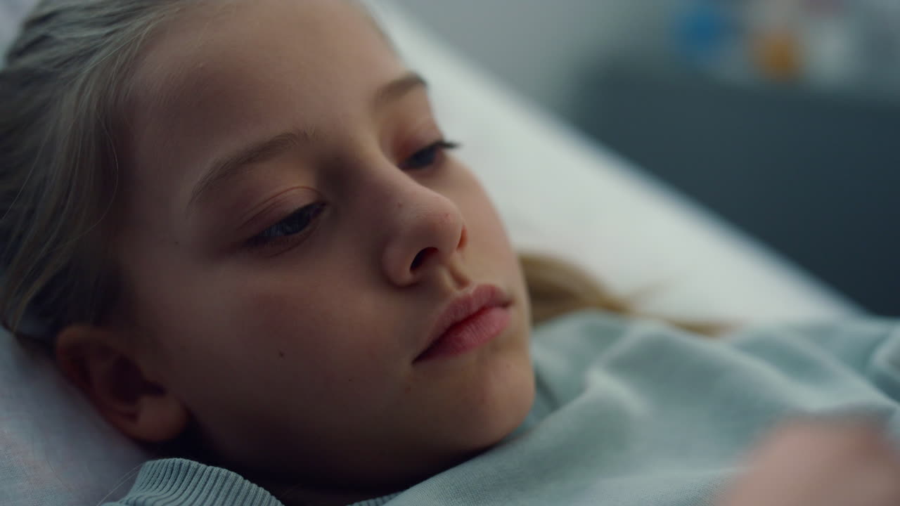 Closeup sick girl lying in hospital bed alone. Bored kid rest in emergency room.