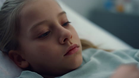 closeup sick girl lying in hospital bed alone. bored kid rest in emergency room.