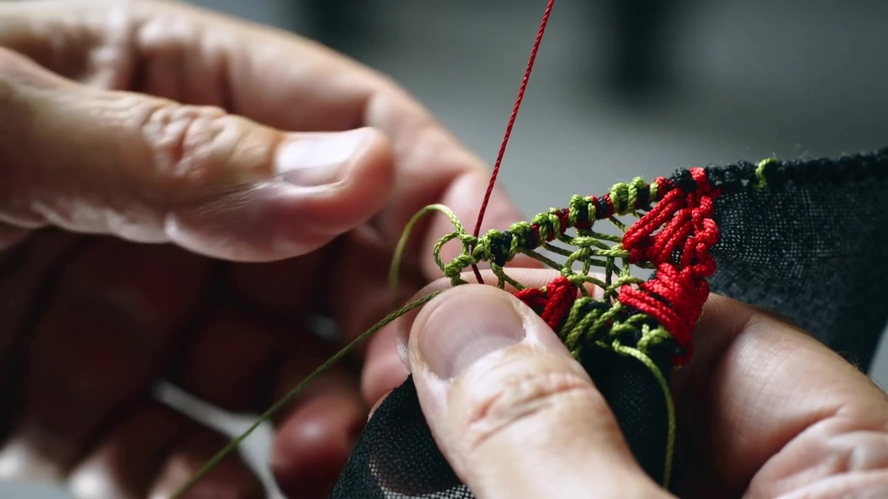 Positioning red cord, pulling adult hands threading through green loops on black edge, forming trim
