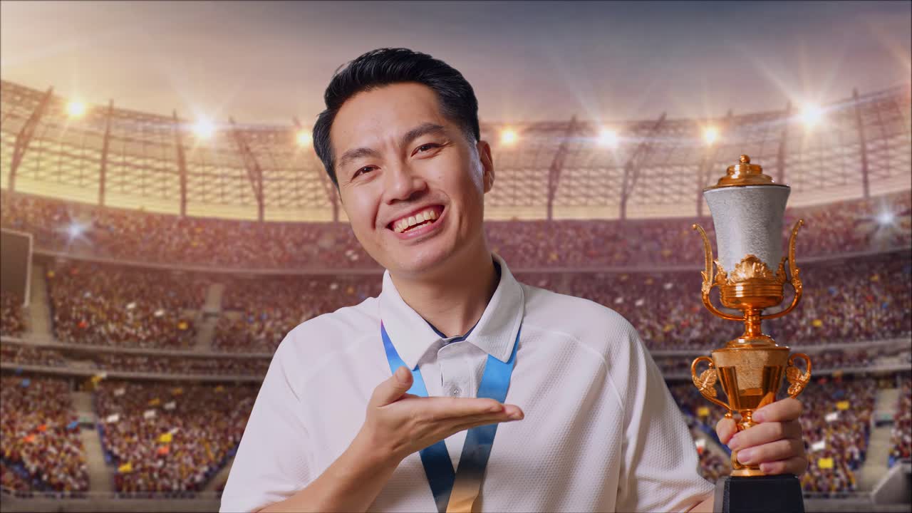 황금 메달을 들고 있는 아시아인 남자가 손에 들고 있는 황금 트로피를 가리키며 미소 짓고 있으며, 경기장에서 첫 번째 우승자로서 자랑스럽게 승리하고 있다.