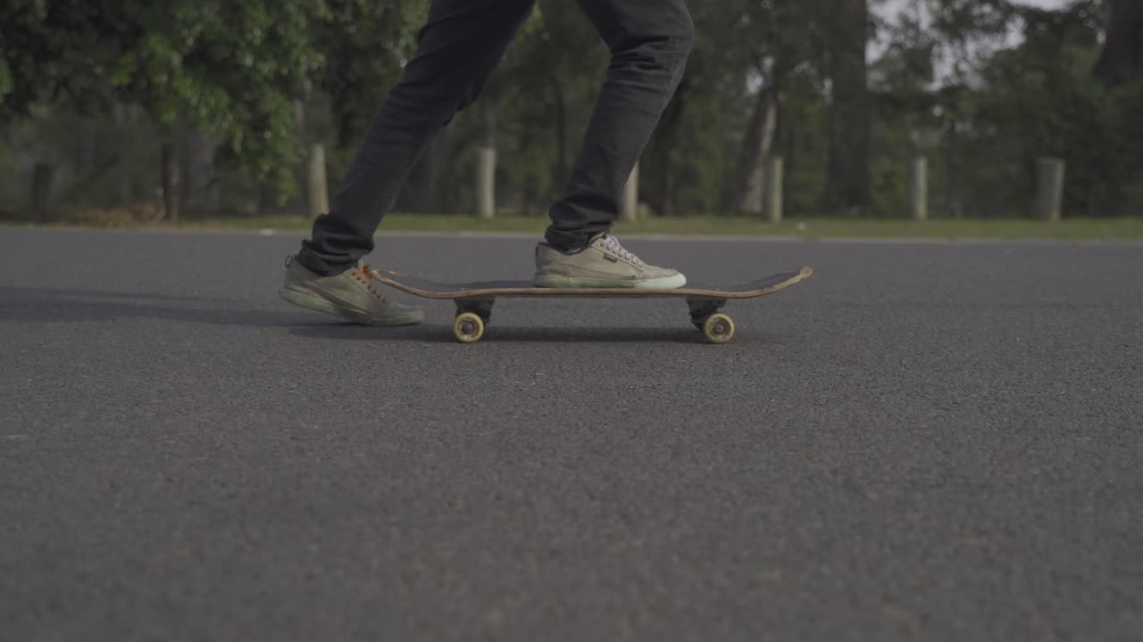 A dynamic ground-level lateral shot following beside a skater as he rides his skateboard and performs kicks to move it around