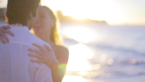 couple turning and kissing during sunset before they walk towards the sea