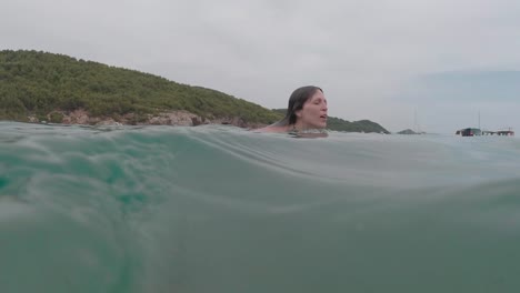 caucasian female swims in translucent water, split shot of underwater and sea surface, slow motion