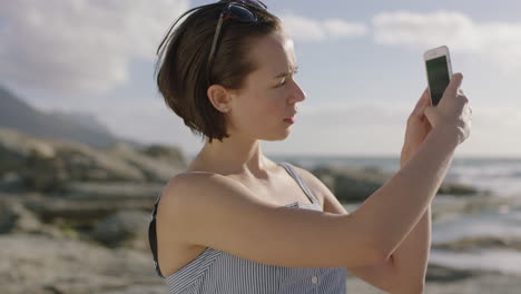 portrait-of-attractive-young-woman-taking-photo-using-smartphone-on-sunny-day-at-beach