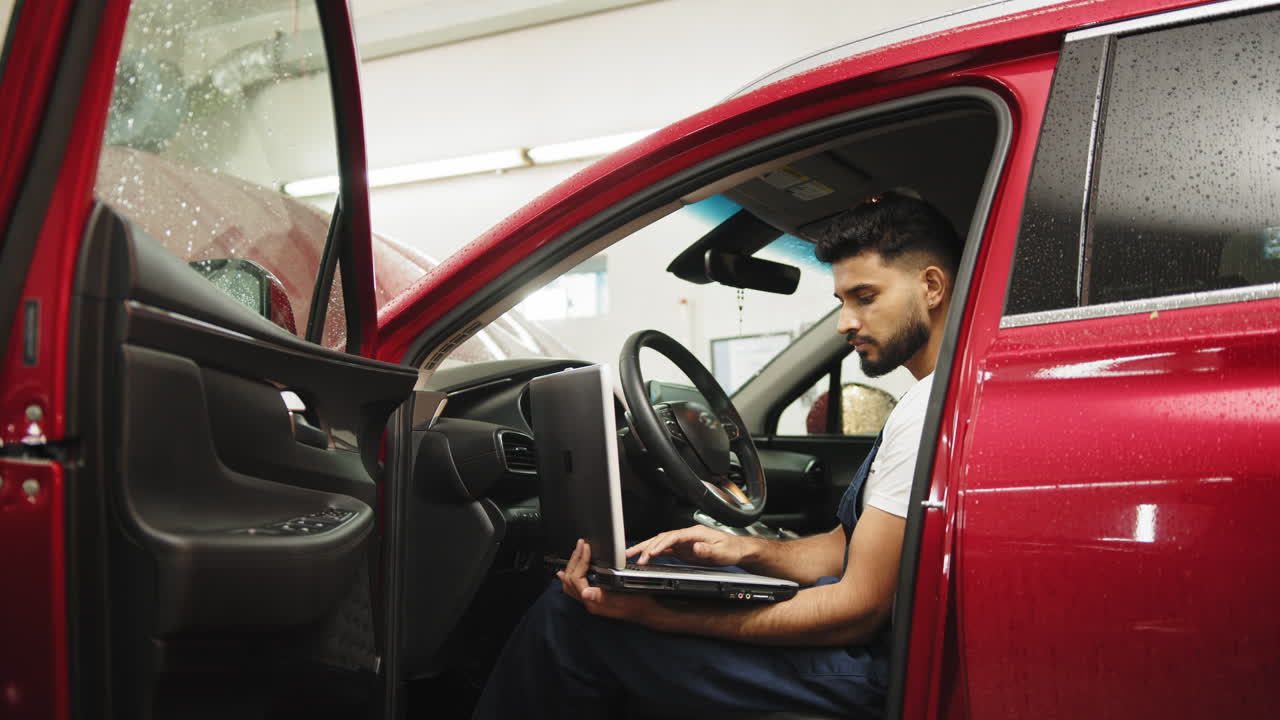 mecánico trabajando en un coche rojo con una computadora portátil