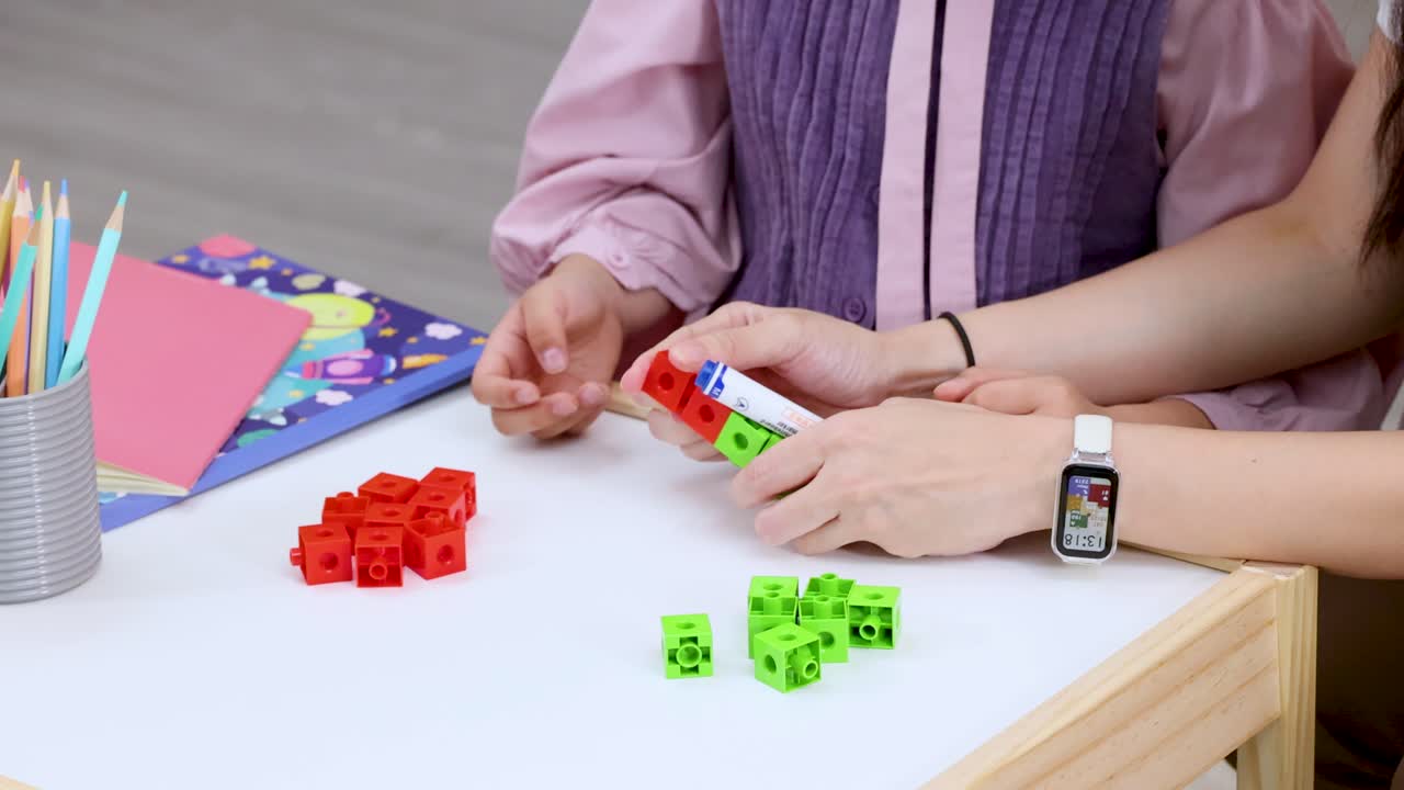 Child and teacher build colored counting cubes at small classroom table with overhead camera