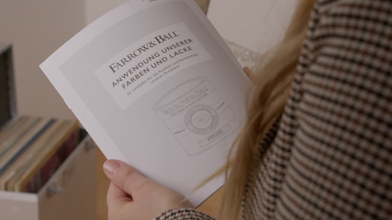High Quality Video of a person holding a Farrow and Ball application guide for paints and finishes. Close-up highlighting instructional content and premium branding
