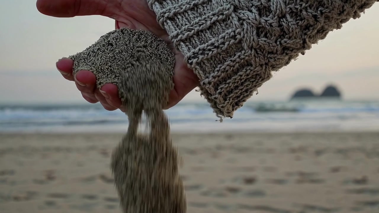 Persona che versa sabbia dalla mano su una spiaggia al tramonto.