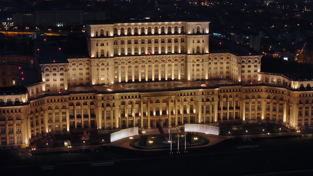 Aerial drone view of illuminated Palace of the Parliament in Bucharest downtown in the evening. Multiple districts around. Romania