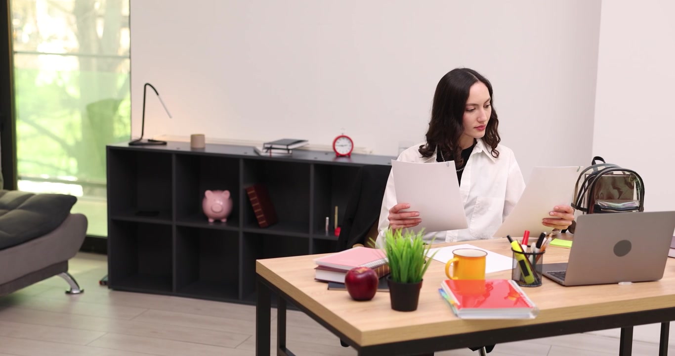 Donna alla scrivania che esamina documenti e confronta i dati sul laptop
