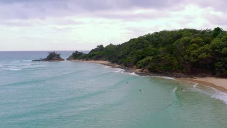 People-enjoying-the-beautiful-clear-blue-waves-of-Byron-Bay,-Australia--aerial