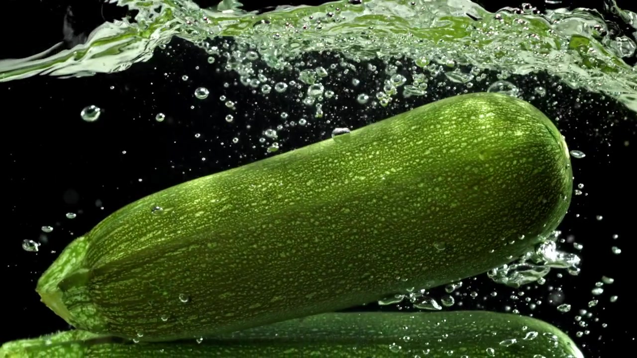 Zucchina verde fresca che si tuffa nell'acqua con bolle su sfondo nero.