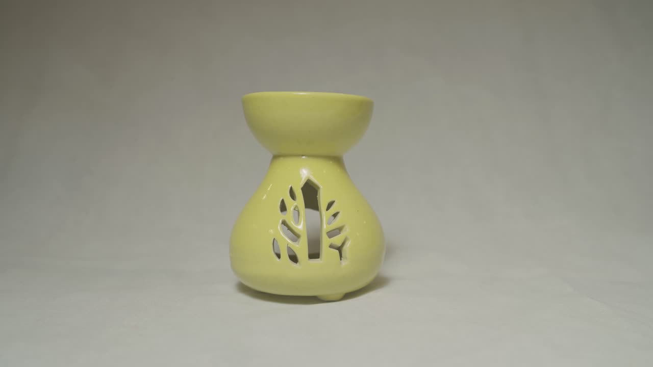 Static shot features yellow ceramic aroma diffuser with decorative tree-shaped cutouts, displayed against plain white backdrop to highlight its form, color, and craftsmanship