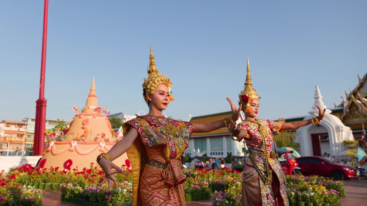 Dos bailarines con elaborados trajes dorados realizan movimientos clásicos de Khon al aire libre durante la hora dorada