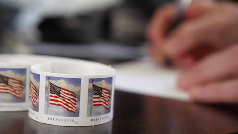 a person addressing and mailing a paper letter with the postal service and using an american flag forever stamp on the white envelope