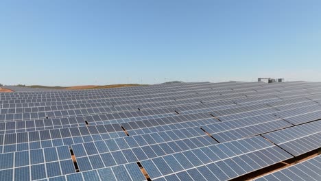 Low-drone-flying-over-solar-panels-farm-fields-with-blue-sky-above