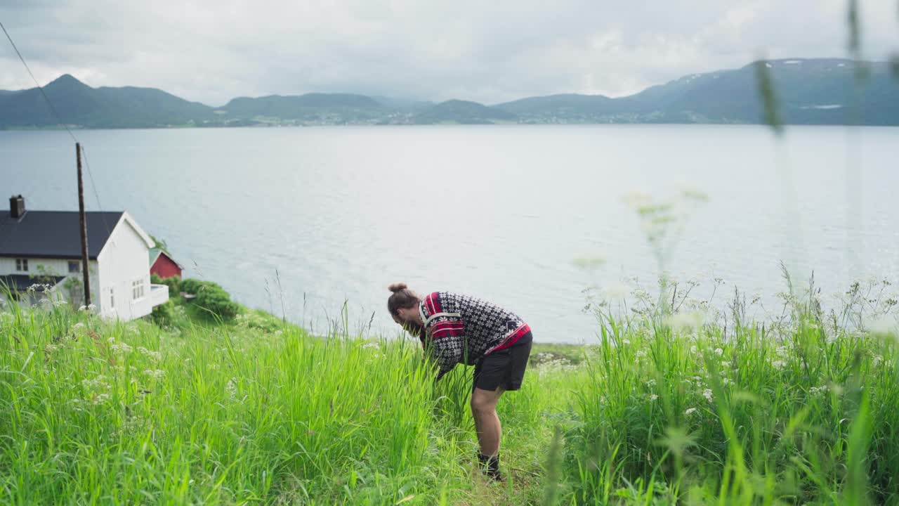 человек собирает урожай среди зеленой травы у берега озера в ветреный день