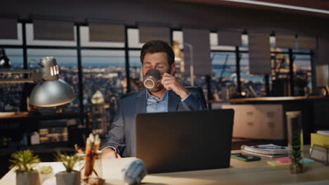 overworked man sipping coffee at night room closeup. businessman looking laptop