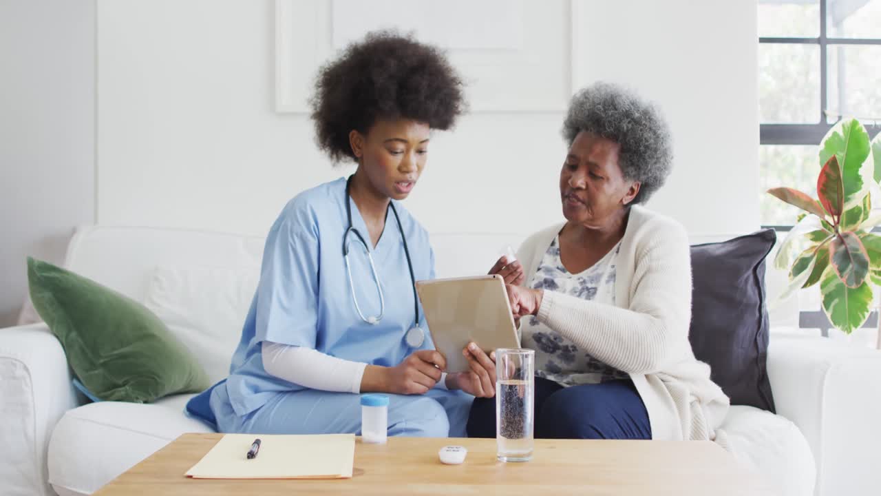Femme médecin afro-américaine et femme âgée discutant et utilisant une tablette.